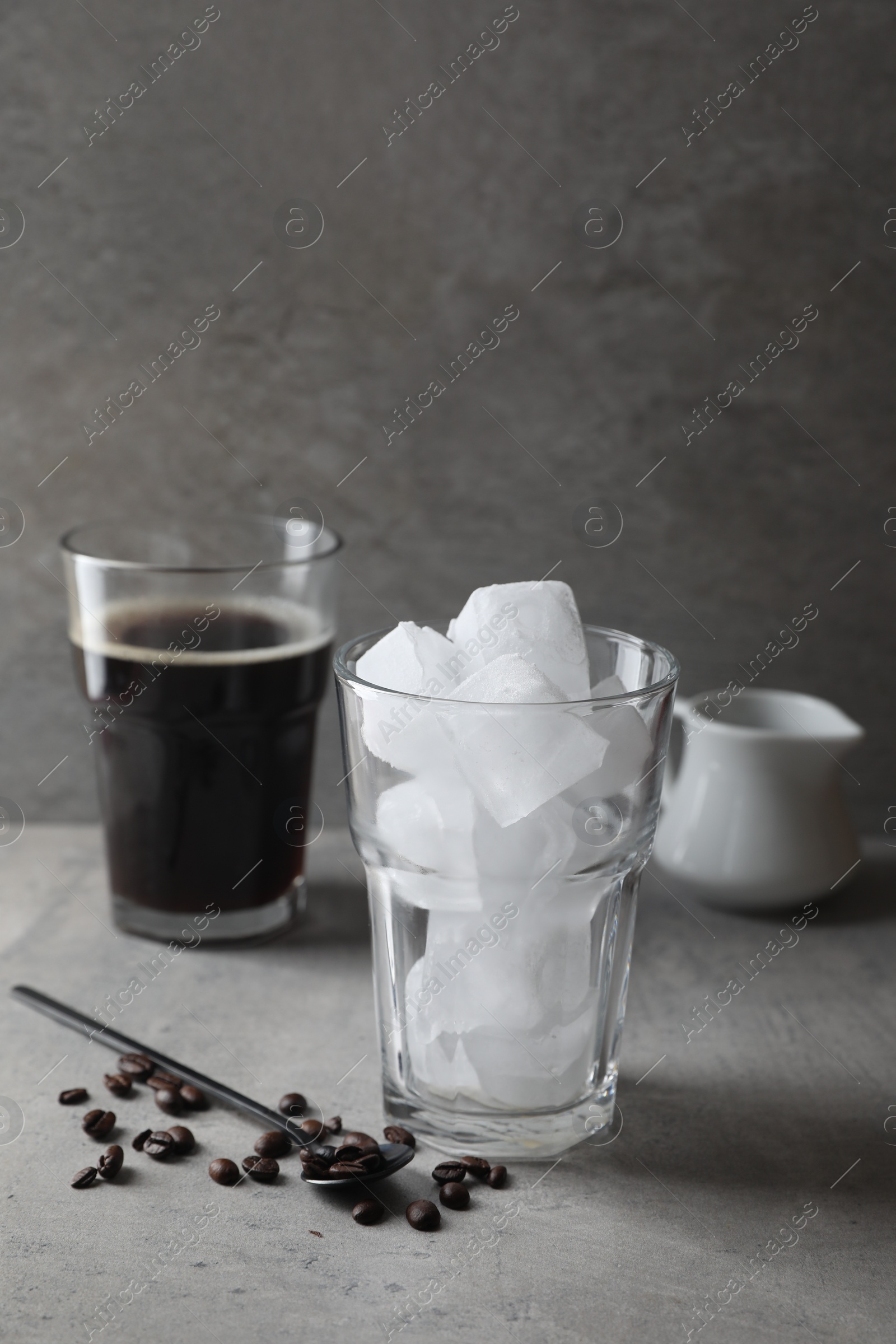 Photo of Making iced coffee. Ice cubes in glass, ingredients and spoon on gray table