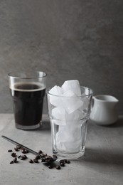 Making iced coffee. Ice cubes in glass, ingredients and spoon on gray table