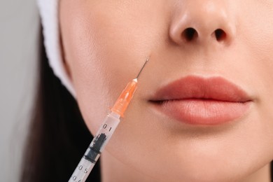 Photo of Young woman getting facial injection on light grey background, closeup. Cosmetic surgery