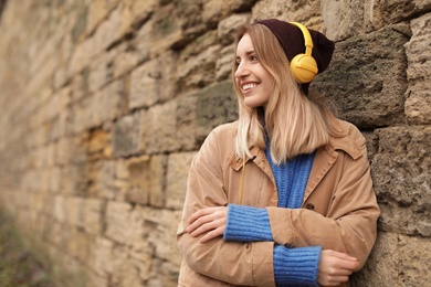Young woman with headphones listening to music near stone wall. Space for text