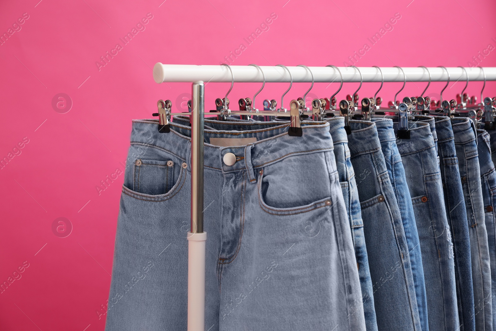 Photo of Rack with stylish jeans on pink background, closeup
