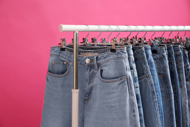 Rack with stylish jeans on pink background, closeup