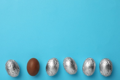 Photo of Chocolate eggs wrapped in foil on light blue background, flat lay. Space for text