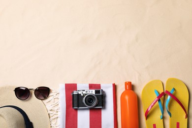 Beach towel, hat, sunglasses, camera, sunscreen and flip flops on sand, flat lay. Space for text