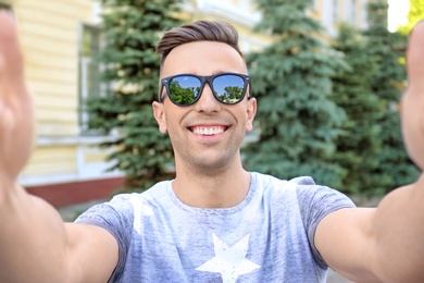 Young man in sunglasses taking selfie outdoors