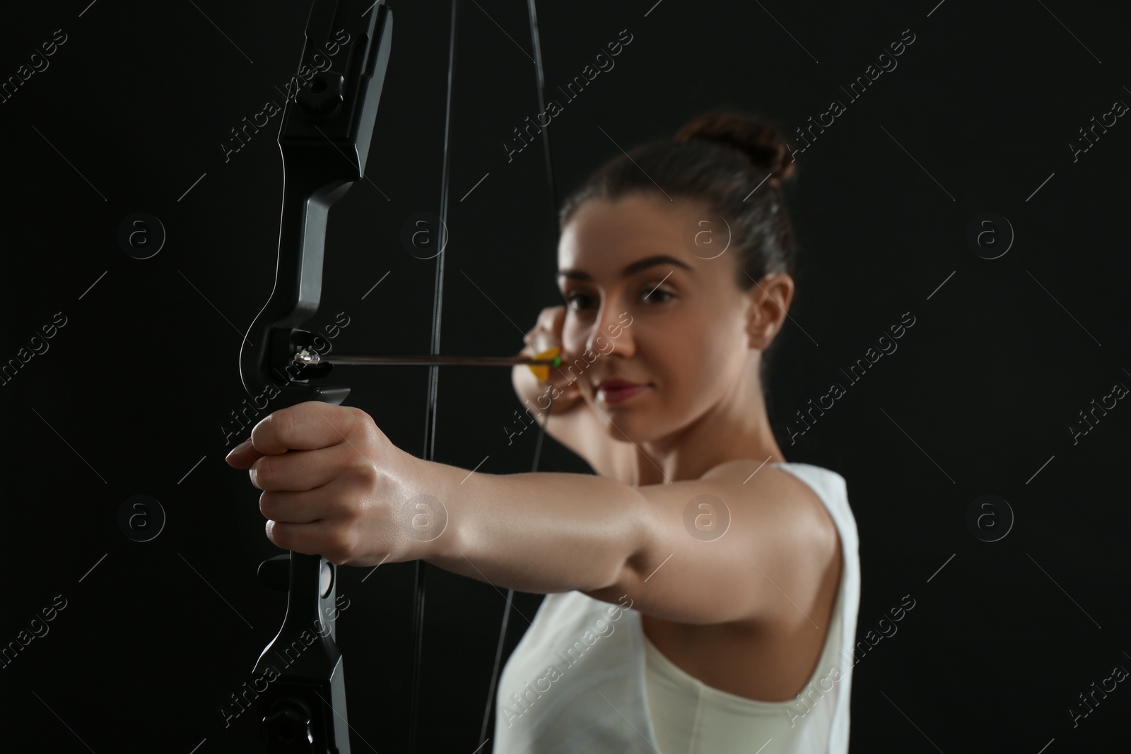 Photo of Woman with bow and arrow practicing archery against black background, focus on hand