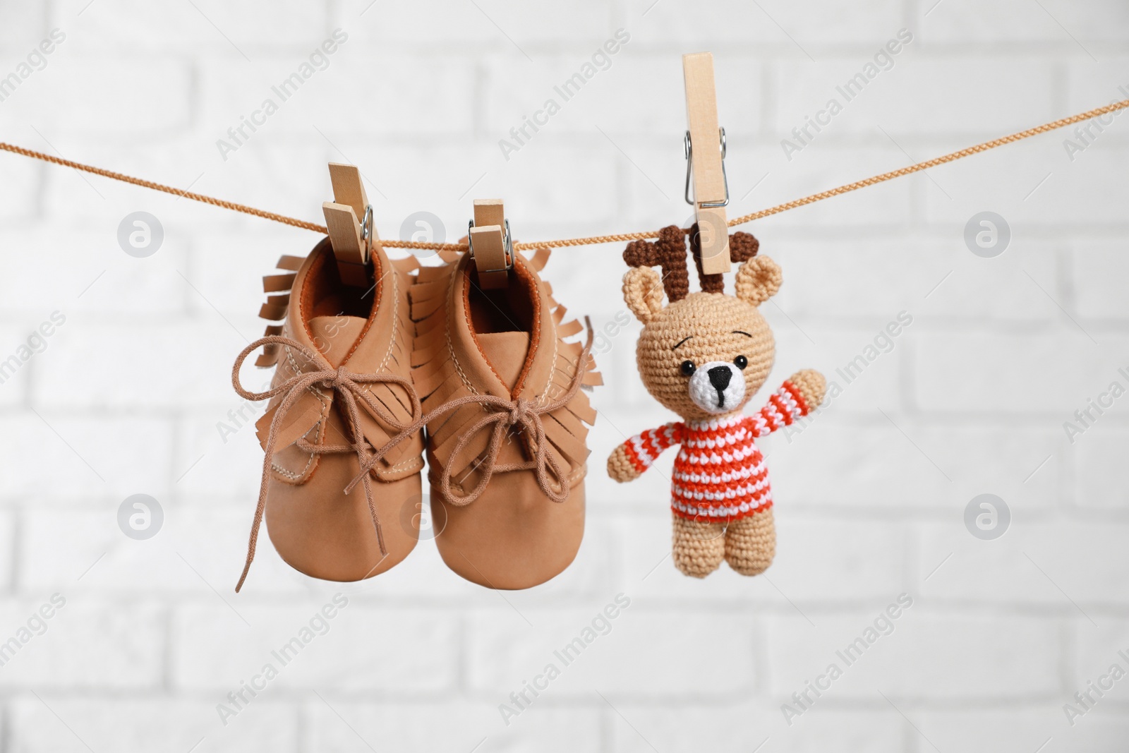 Photo of Cute baby shoes and crochet toy drying on washing line against white brick wall