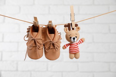 Cute baby shoes and crochet toy drying on washing line against white brick wall