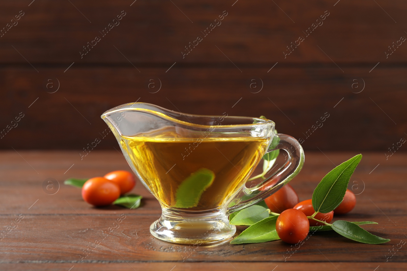 Photo of Glass sauce boat with jojoba oil and seeds on wooden table