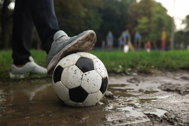 Photo of Man with dirty soccer ball in puddle outdoors, closeup
