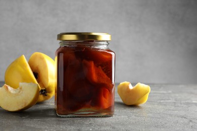 Photo of Tasty homemade quince jam in jar and fruits on grey textured table. Space for text