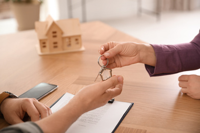 Photo of Real estate agent giving key with trinket to client in office, closeup