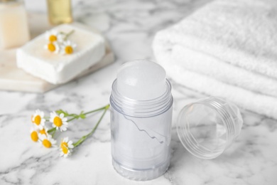 Photo of Natural crystal alum deodorant and chamomile flowers on white marble background