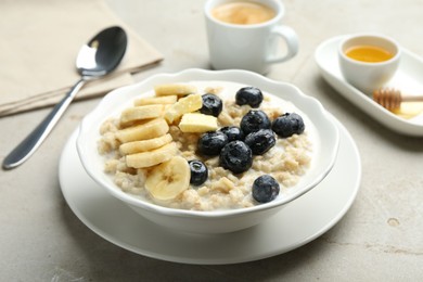 Tasty oatmeal with banana, blueberries, butter and milk served in bowl on light grey table