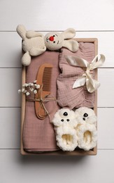Photo of Crate with children's clothes, shoes, toy, pacifier and comb on white wooden table, top view