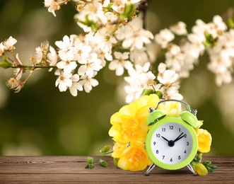 Image of Alarm clock and spring flowers on wooden table, space for text. Time change 