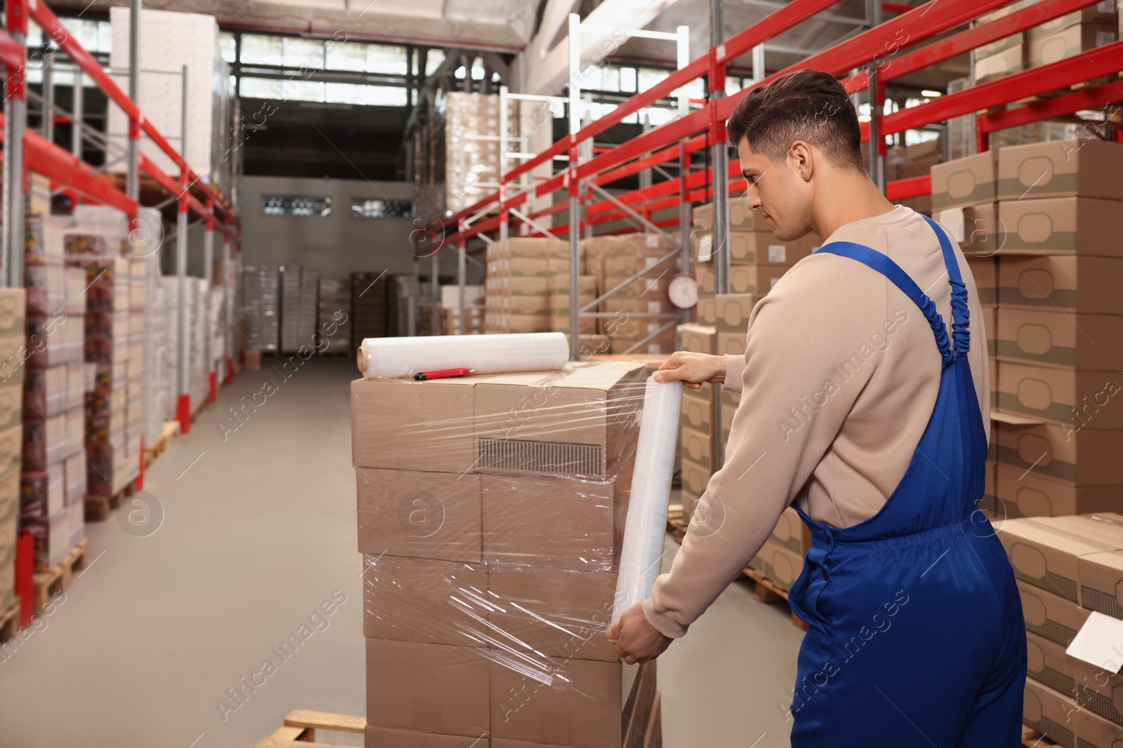 Photo of Worker wrapping boxes in stretch film at warehouse