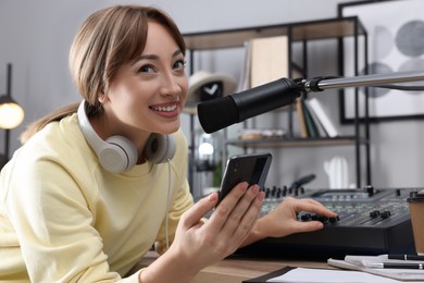 Woman with smartphone working as radio host in modern studio
