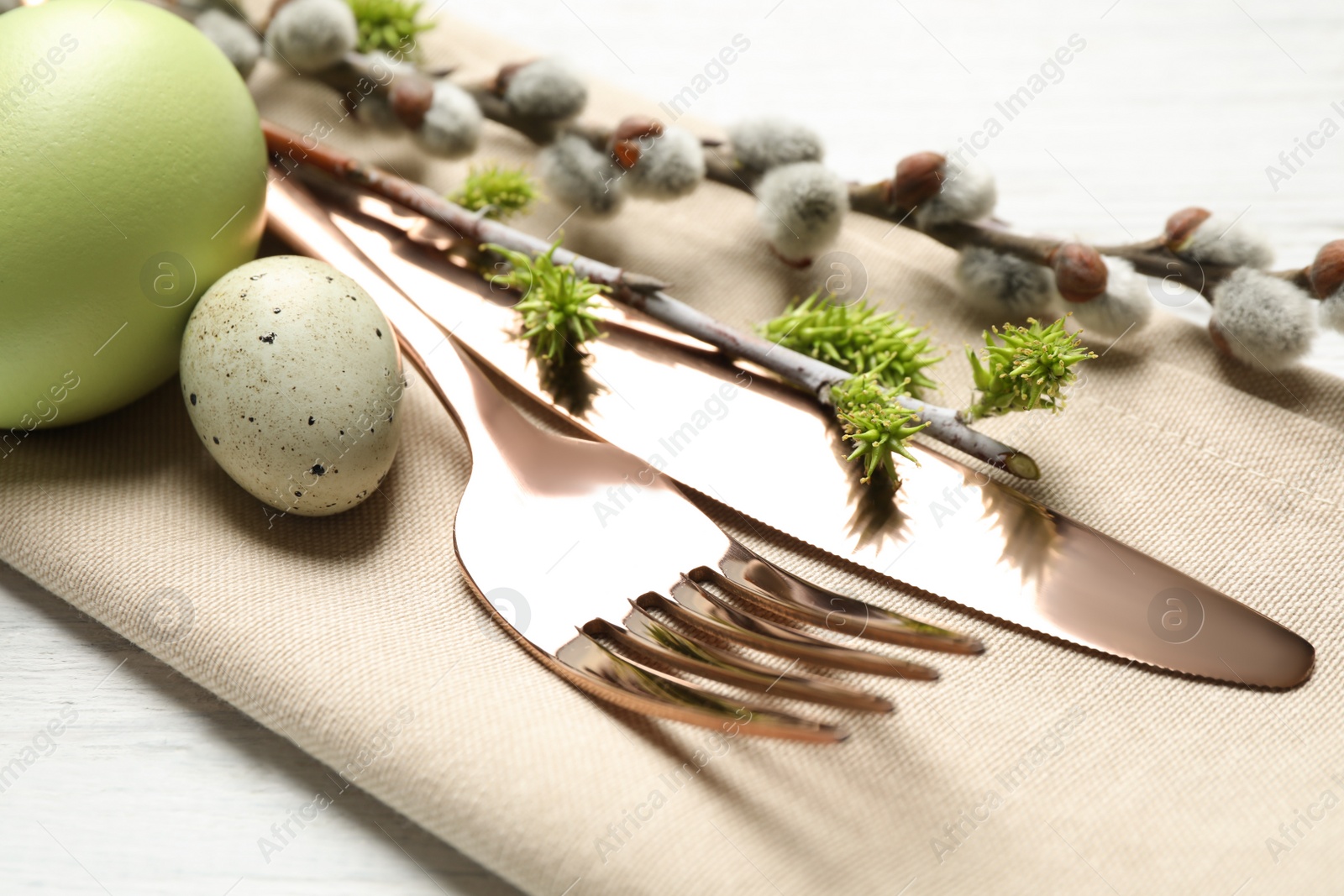 Photo of Cutlery set with beautiful willow branches on white wooden table, closeup. Easter celebration