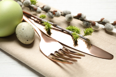 Cutlery set with beautiful willow branches on white wooden table, closeup. Easter celebration