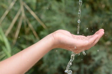 Photo of Pouring water into kid`s hand outdoors, closeup