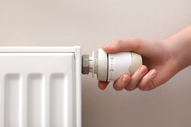 Photo of Girl adjusting heating radiator thermostat near white wall, closeup