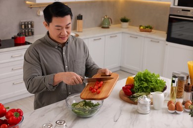 Photo of Cooking process. Man adding cut tomatoes into bowl at countertop in kitchen