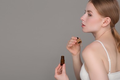 Photo of Beautiful young woman applying essential oil onto shoulder on grey background. Space for text