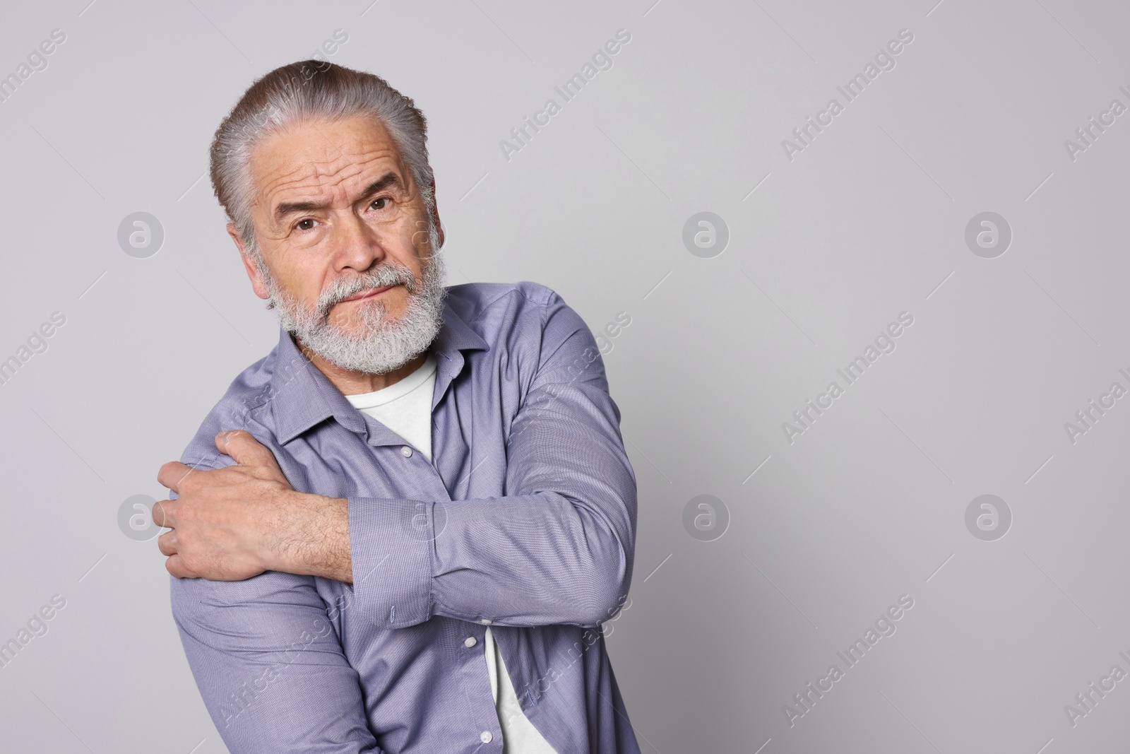 Photo of Senior man suffering from pain in shoulder on light grey background, space for text. Arthritis symptoms