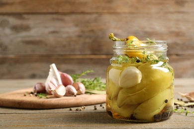 Glass jar with pickled peppers on wooden table. Space for text