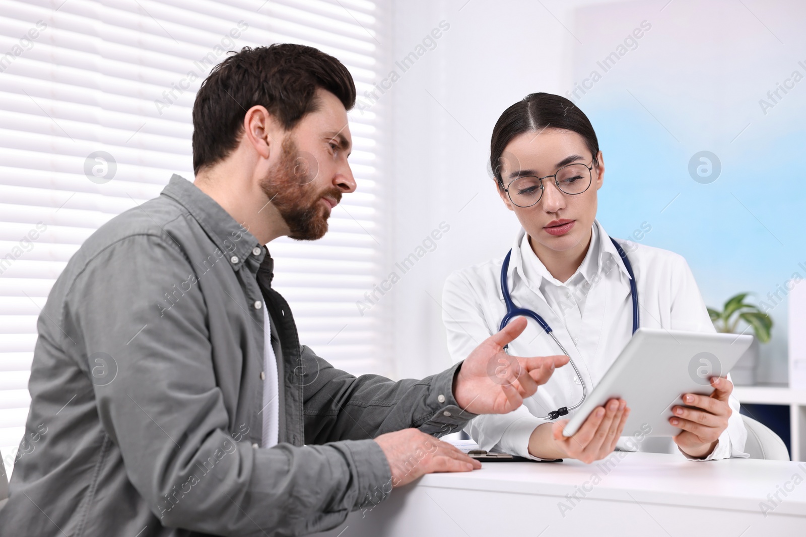 Photo of Doctor with tablet consulting patient during appointment in clinic