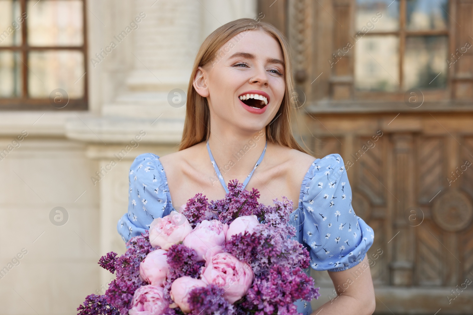 Photo of Beautiful woman with bouquet of spring flowers near building outdoors