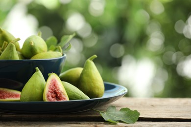 Cut and whole green figs on wooden table against blurred background, space for text