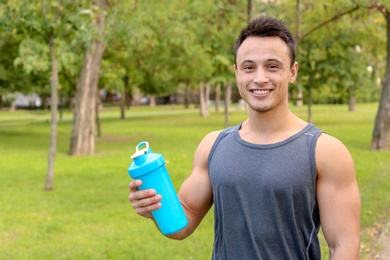 Man with bottle of protein shake in park. Space for text