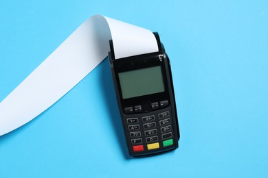 Photo of Payment terminal with thermal paper for receipt on light blue background, top view