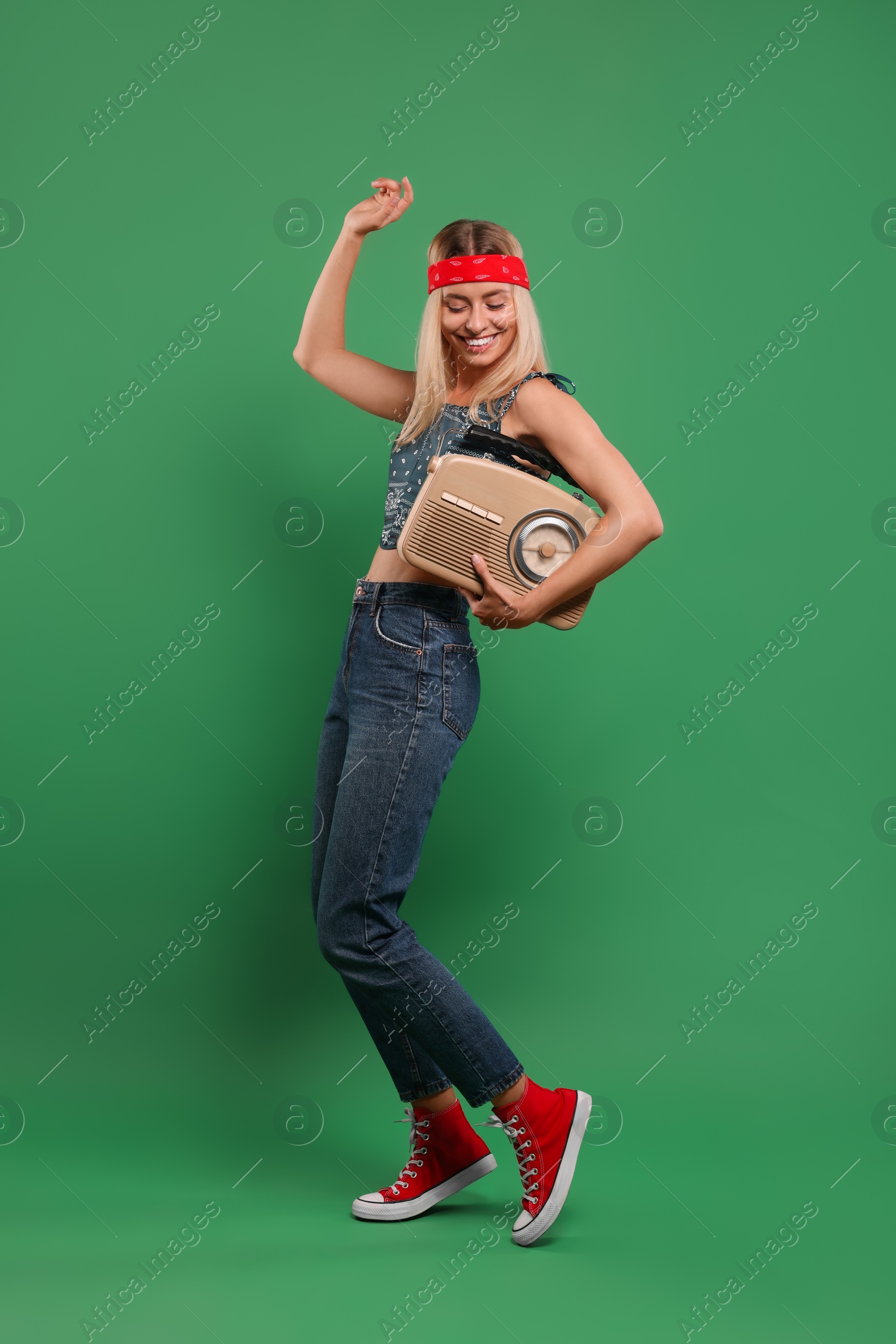 Photo of Happy hippie woman with retro radio receiver dancing on green background