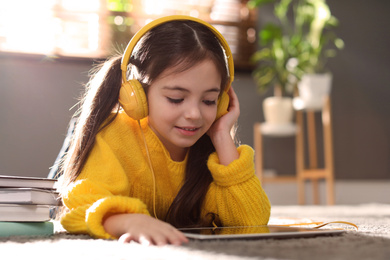 Photo of Cute little girl with headphones and tablet listening to audiobook at home