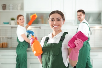 Photo of Portrait of young woman with sprayer and rag in kitchen. Cleaning service
