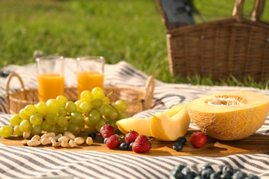 Photo of Picnic blanket with delicious food and juice on green grass outdoors