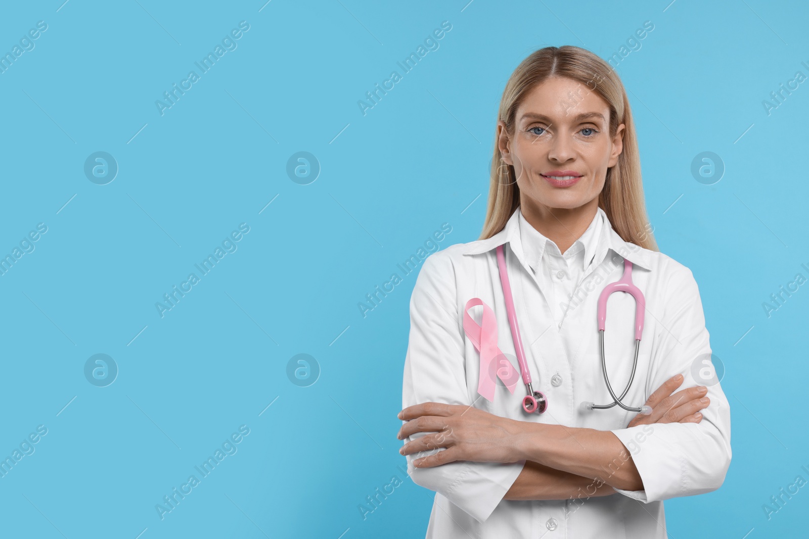 Photo of Doctor with pink ribbon and stethoscope on light blue background, space for text. Breast cancer awareness