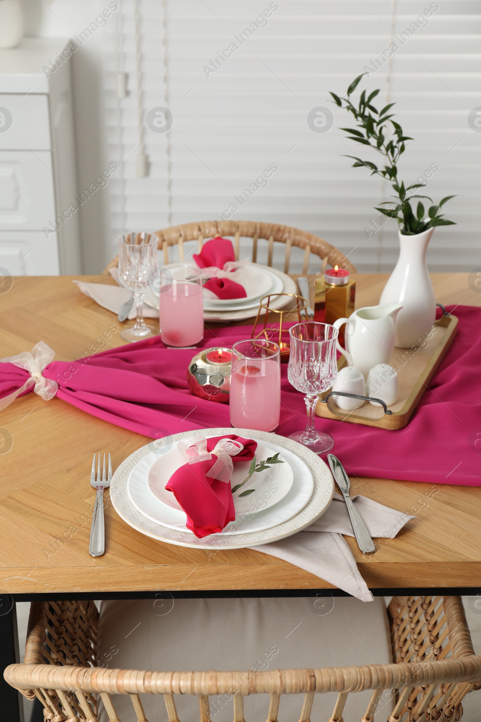 Photo of Color accent table setting. Glasses, plates, pink napkins and vase with green branch in dining room