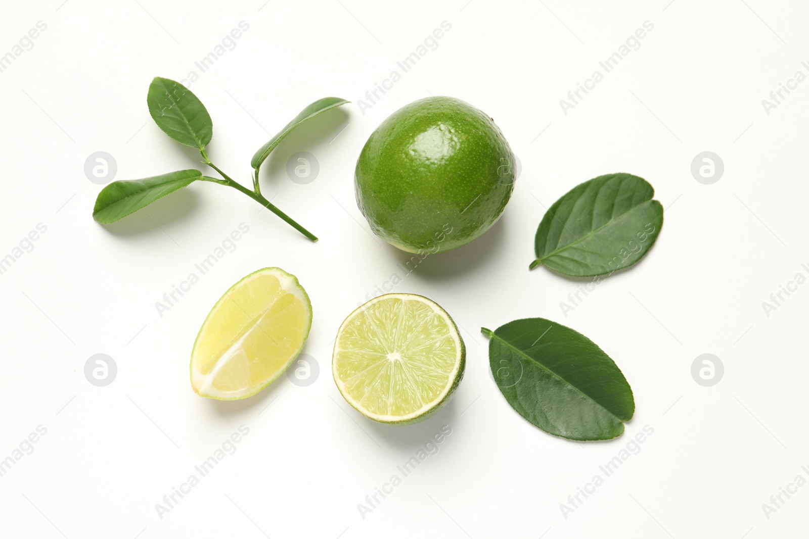 Photo of Whole and cut fresh ripe limes with green leaves on white background, flat lay