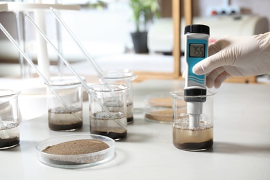 Photo of Scientist measuring acidity and pH of soil at table, closeup. Laboratory analysis