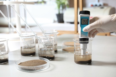 Scientist measuring acidity and pH of soil at table, closeup. Laboratory analysis