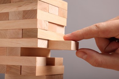 Playing Jenga. Man removing wooden block from tower on grey background, closeup