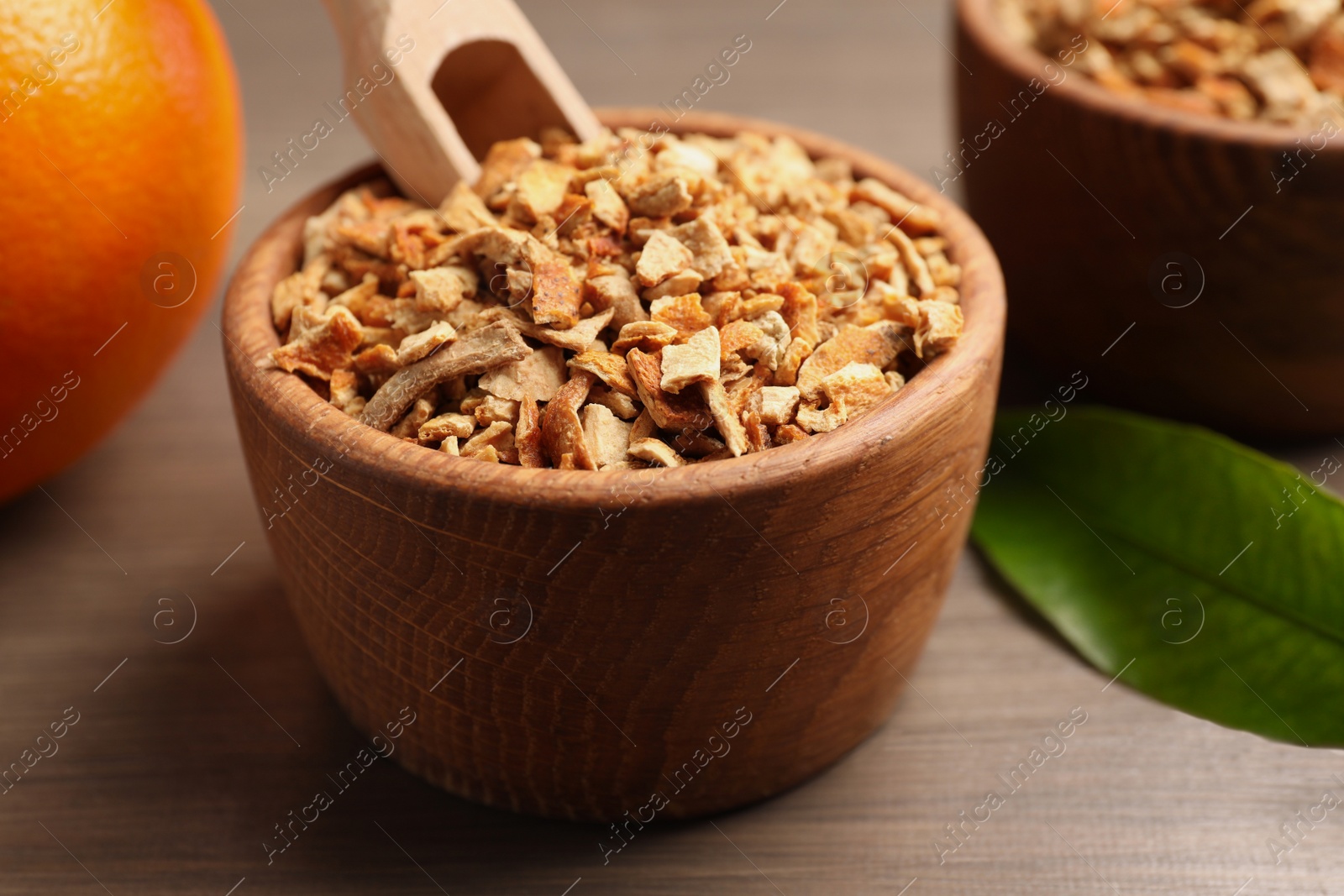 Photo of Bowl of dried orange zest seasoning on wooden table, closeup