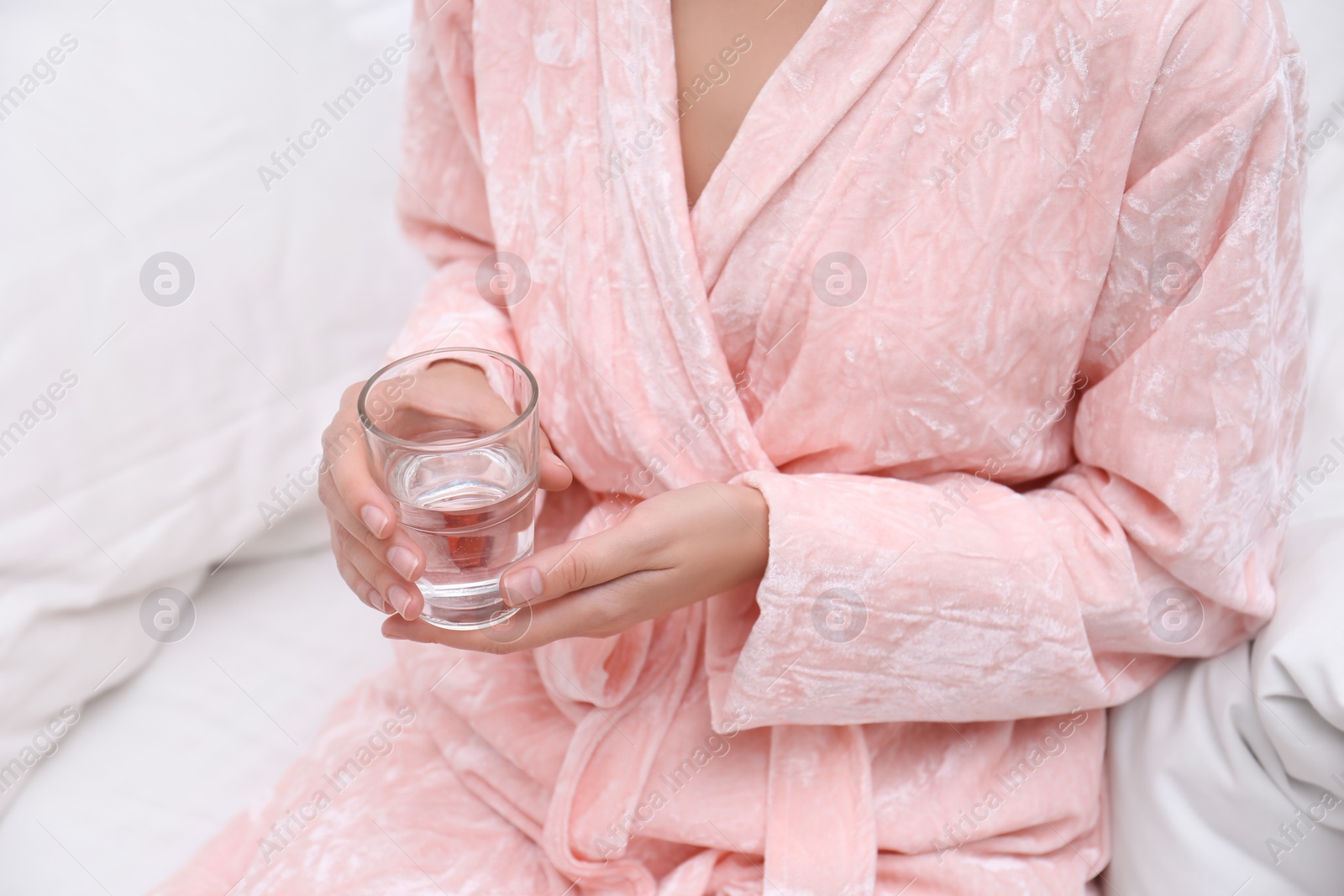 Photo of Woman holding glass of water in bedroom, closeup