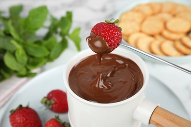 Photo of Fondue pot with chocolate and strawberry on table, closeup