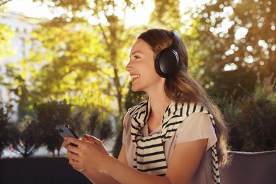 Photo of Smiling woman in headphones using smartphone outdoors