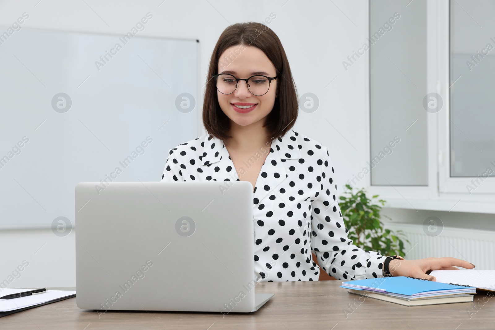 Photo of Happy young intern working with laptop at table in modern office